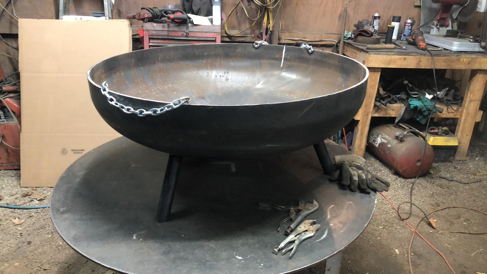 Steel fire pit with a welded chain bail across the rim for lifting